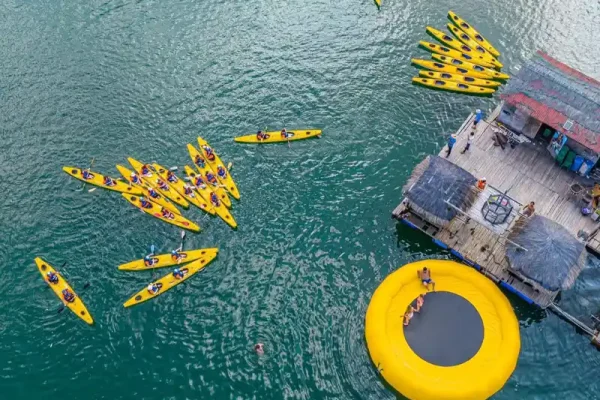 Aerial view of people kayaking near a floating dock and a large yellow water trampoline on the sea