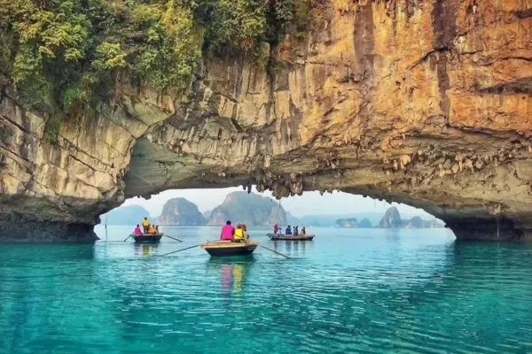 Wooden boat with tourists rowing through limestone arch over emerald sea